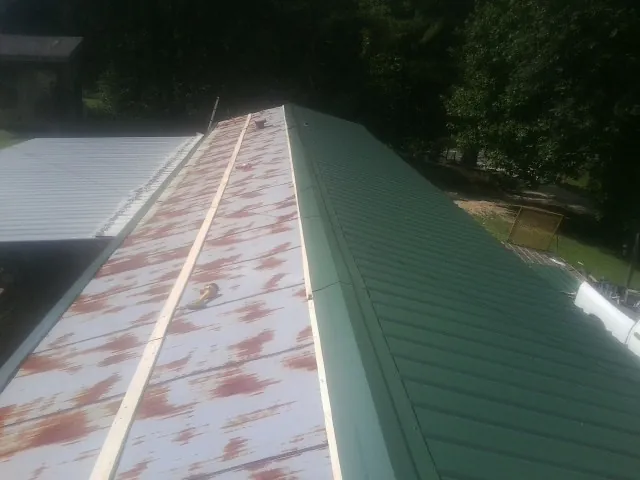 Old rusted panels beside newly installed green metal roofing — Wind Damage Roof Repair by Roofing Brothers in Modoc