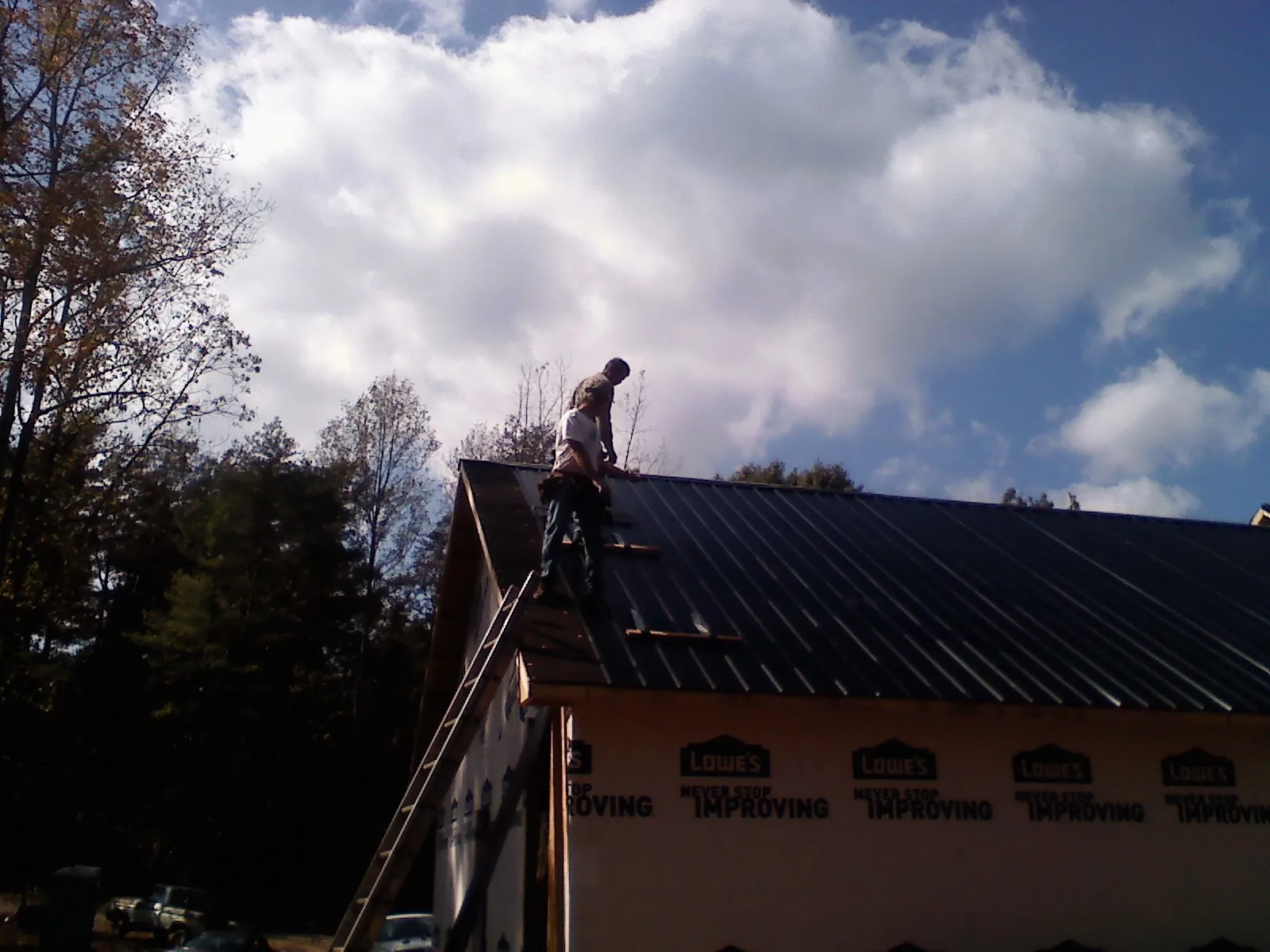 Roofer fastening dark metal panels high against a cloudy sky, from a Roof Inspection job in Modoc