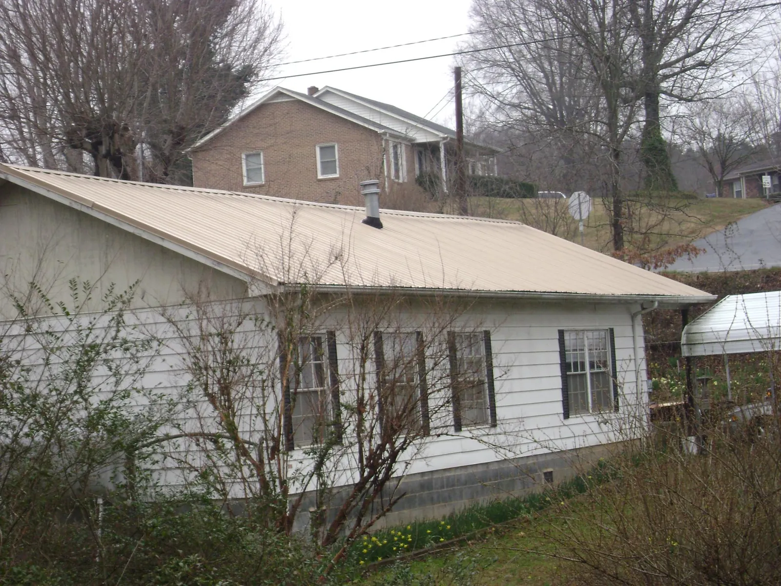 Tan metal roof on a white sided house set into a hillside — Commercial Roofing by Roofing Brothers in Modoc
